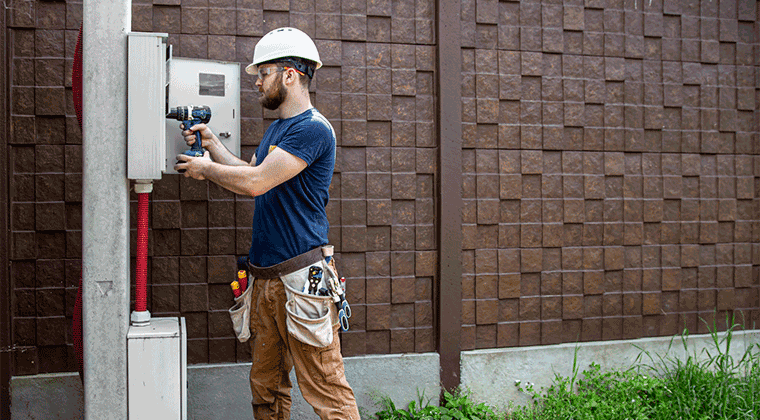 Um homem com capacete está consertando uma rede de eletricidade